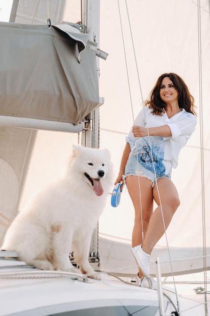 Una mujer feliz con un gran perro blanco en un yate blanco en el mar.