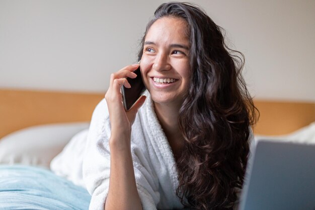 Mujer feliz hablando con celular en el dormitorio en casa