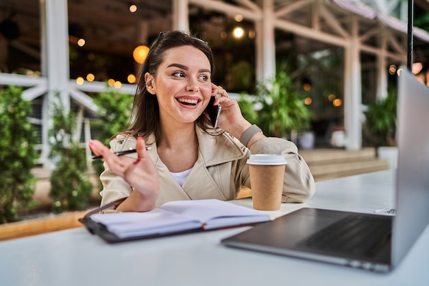 Mujer feliz hablando por teléfono móvil al aire libre y trabajando.