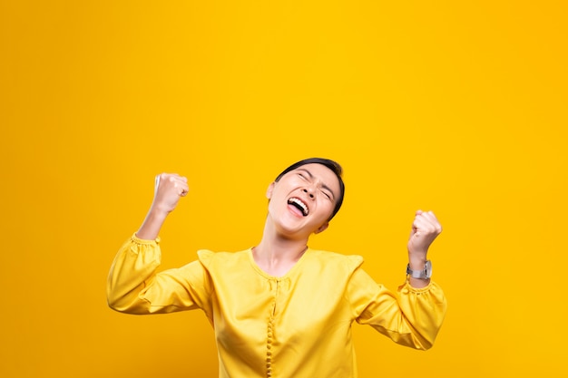 Mujer feliz hacer gesto ganador aislado sobre pared amarilla