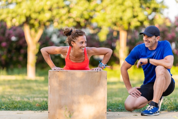 Mujer feliz haciendo flexiones y trabajando en el parque. El hombre es su entrenador físico.