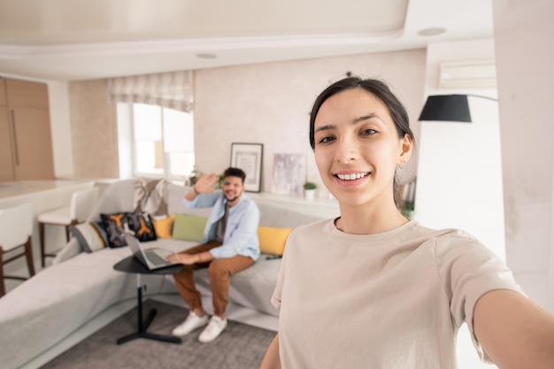 Mujer feliz haciendo selfie con su marido en el fondo en el entorno hogareño