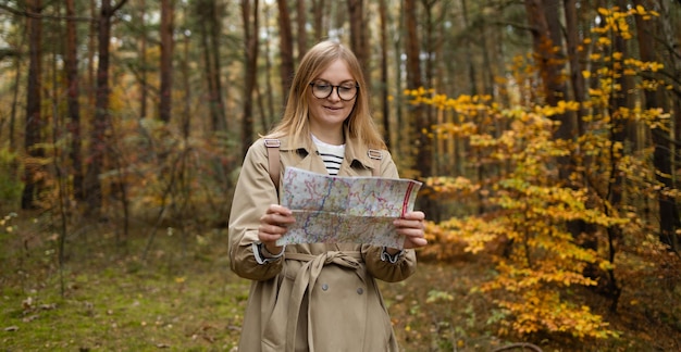 Mujer feliz haciendo senderismo y mirando el mapa al aire libre en la naturaleza, los viajeros exploran el bosque montañoso ma