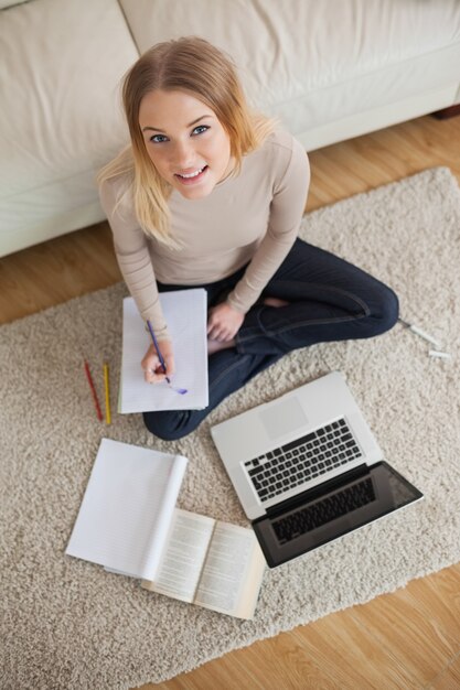 Mujer feliz haciendo la tarea y sentado en el piso usando la computadora portátil