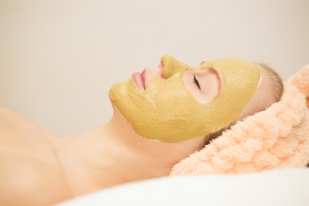 Mujer feliz hermosa en el balneario que hace el tratamiento de la mascarilla. Foco selectivo