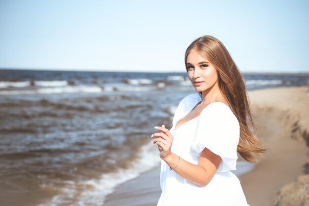 Mujer feliz y hermosa en la playa del océano de pie en un vestido blanco de verano