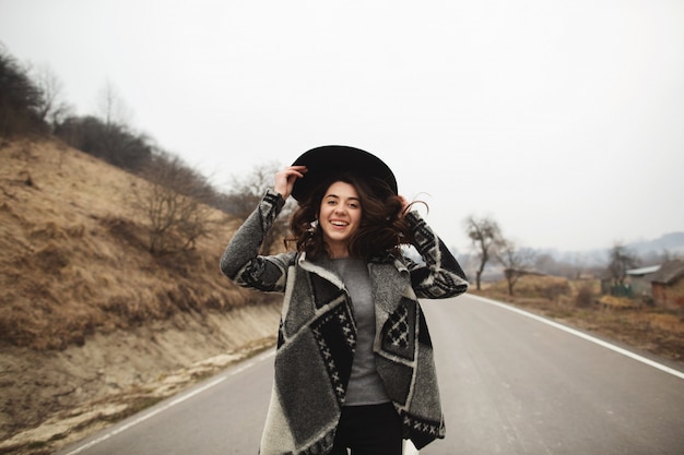 Mujer feliz en un hermoso cárdigan gris y sombrero negro cabalga por el camino
