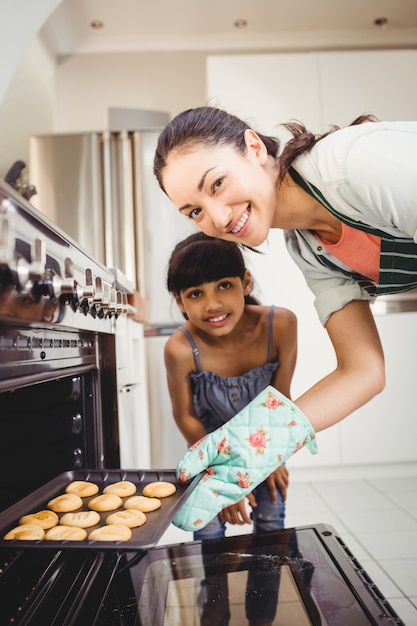 Mujer feliz con hija colocando galletas en el horno