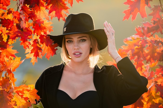 Mujer feliz con hojas de otoño en la cara en otoño retrato de una mujer joven con arce de otoño