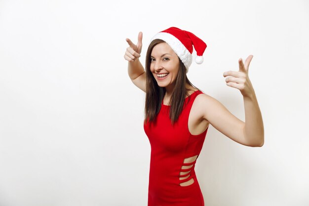 Mujer feliz joven bastante caucásica con sonrisa encantadora con vestido rojo y sombrero de Navidad extendiendo las manos aisladas sobre fondo blanco. Santa niña. Vacaciones de año nuevo 2018. Copie el espacio para publicidad