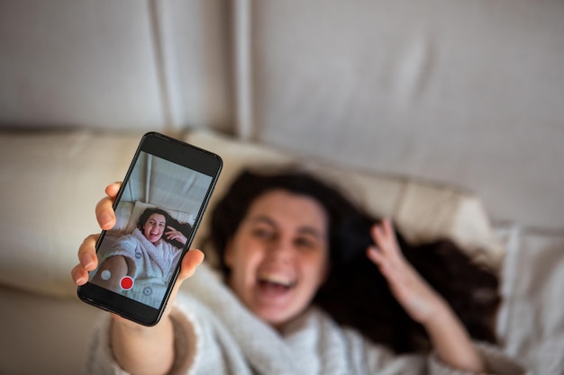 Mujer feliz joven que toma la historia del selfie que se acuesta en la cama