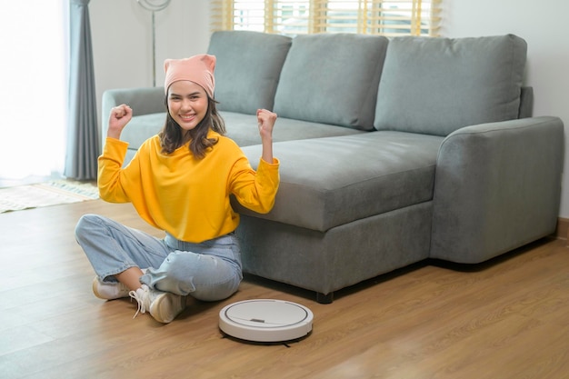 Mujer feliz joven que usa la aspiradora robótica en sala de estar
