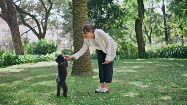Mujer feliz jugando al caniche en la hierba verde del parque chica con un cachorro negro peludo