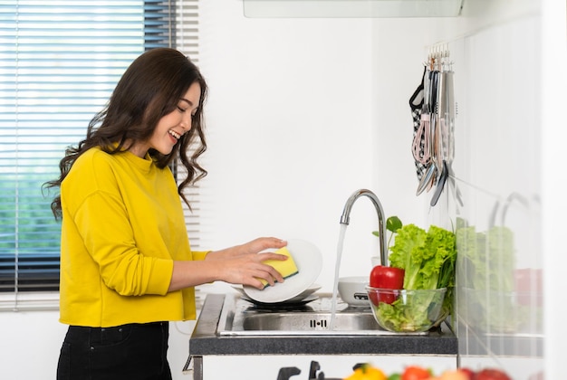 Mujer feliz lavando platos en el fregadero de la cocina en casa