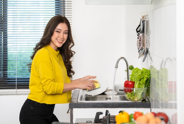 Mujer feliz lavando platos en el fregadero de la cocina en casa