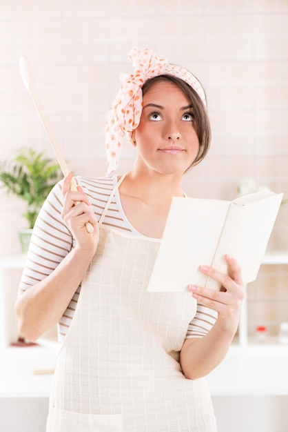 Mujer feliz leyendo libros de cocina y pensando en la cocina