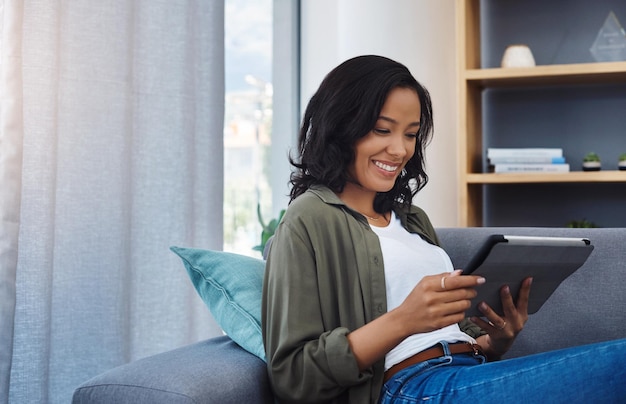 Mujer feliz libro electrónico o tableta en el sofá para leer investigación de blog en línea o artículo en redes sociales en el hogar Decoración de interiores de noticias o chica en tecnología de pantalla táctil para la renovación en una casa moderna