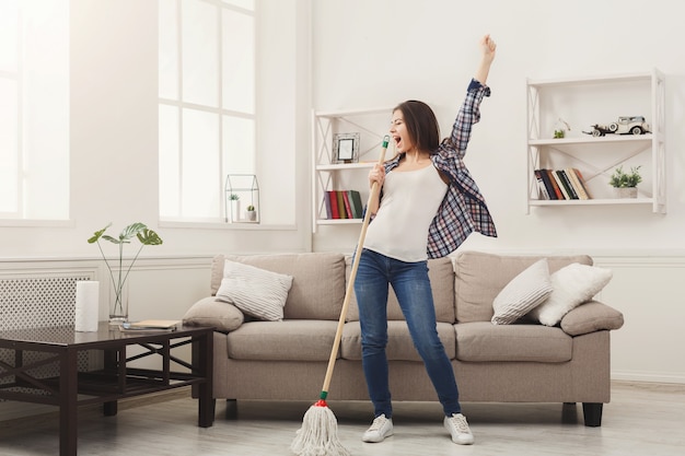 Mujer feliz limpiando la casa con un trapeador y divirtiéndose