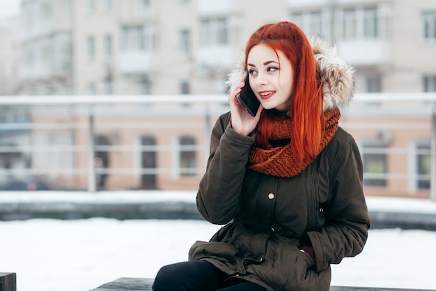 Mujer feliz llamando al teléfono móvil en la calle en invierno