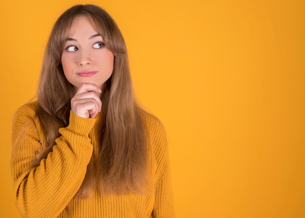 Mujer feliz con las manos en el mentón sobre fondo amarillo