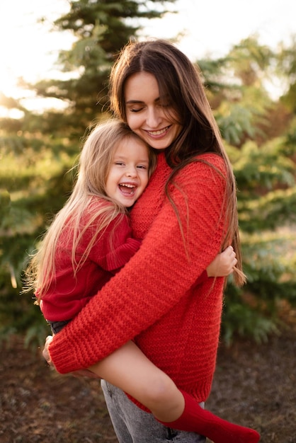 Mujer feliz mantenga niño niña use suéteres rojos brillantes posando sobre fondo de naturaleza