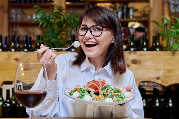 Foto mujer feliz de mediana edad comiendo ensalada en un restaurante cara alegre de primer plano