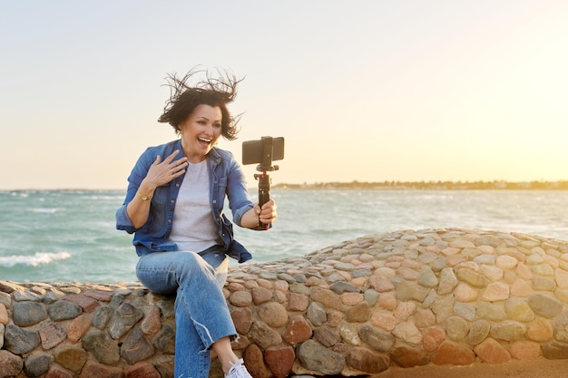 Mujer feliz de mediana edad hablando en línea grabando video en un teléfono inteligente