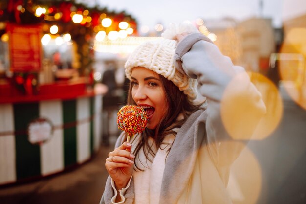 Mujer feliz en el mercado navideño con manzana caramelizada Actividades al aire libre en Navidad