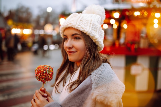 Mujer feliz en el mercado navideño con manzana caramelizada Actividades al aire libre en Navidad