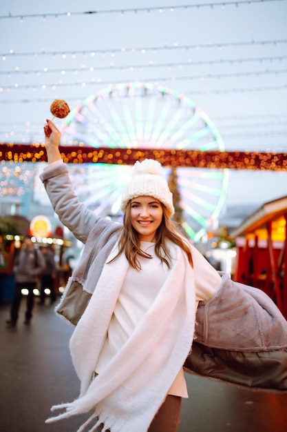 Mujer feliz en el mercado navideño con manzana caramelizada Actividades al aire libre en Navidad