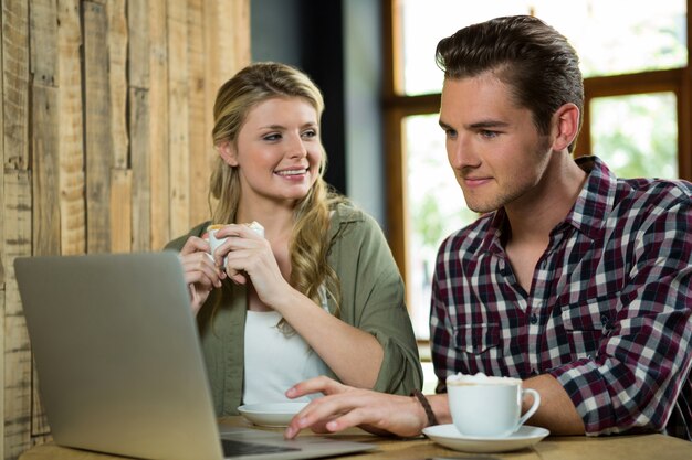 Mujer feliz mirando al hombre usando la computadora portátil en la cafetería.