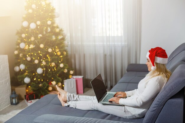 Mujer feliz mirando en la computadora portátil delante del árbol de Navidad