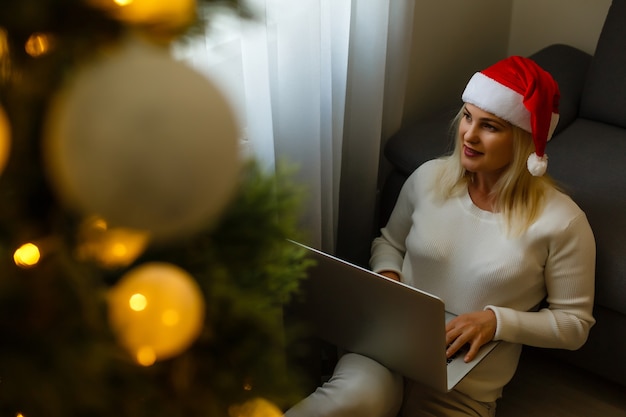 Mujer feliz mirando en la computadora portátil delante del árbol de Navidad