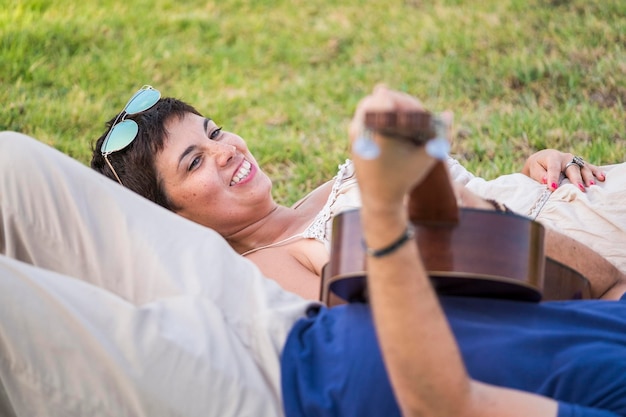 Mujer feliz mirando a un hombre tocando la guitarra mientras está acostado en el parque