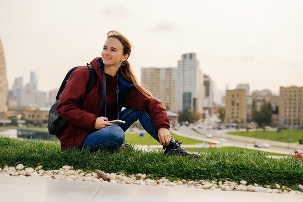 Mujer feliz con una mochila se sienta en un fondo de edificio