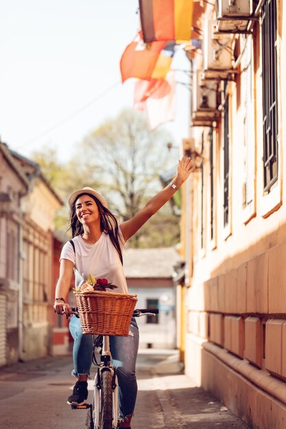 Mujer feliz montando en bicicleta por la calle de la ciudad, en un día soleado de verano, sonriendo de alegría durante la actividad al aire libre.