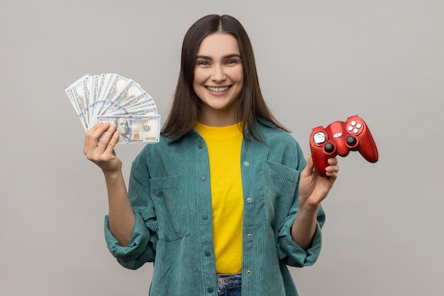 Mujer feliz mostrando a la cámara joypad rojo y billetes de dólares jugando y ganando dinero