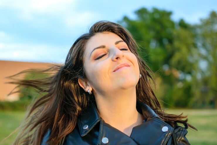 Mujer feliz moviendo la cabeza con satisfacción al sol con cabello castaño y ojos cerrados