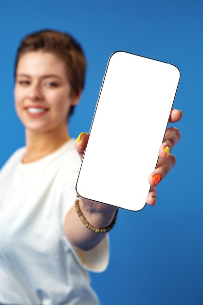 Mujer feliz muestra la pantalla del teléfono inteligente en blanco contra el fondo azul.