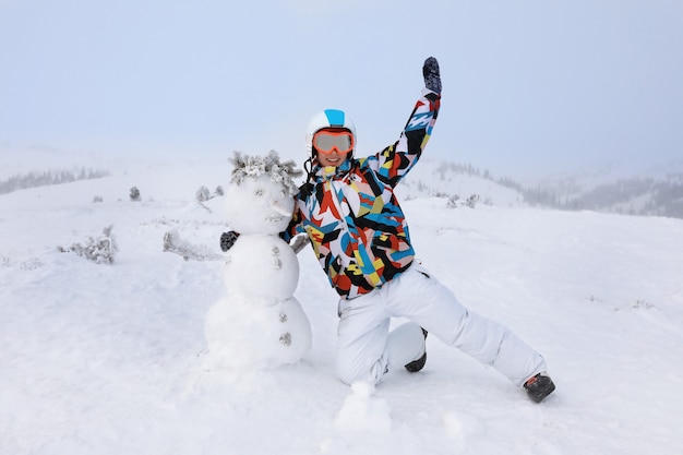 Mujer feliz con muñeco de nieve en el resort. Vacaciones de invierno