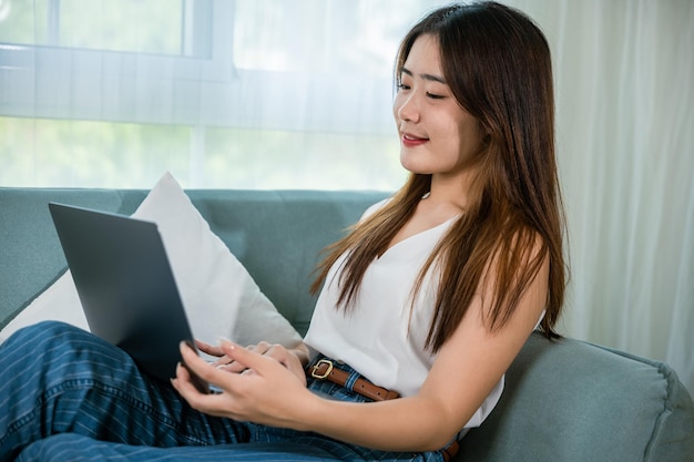 Mujer feliz navegando por Internet durante su tiempo libre en una computadora portátil Mujer sonriente sentada en el sofá usando una computadora portátil en la sala de estar en casa chica de compras o chateando en línea en la red de redes sociales