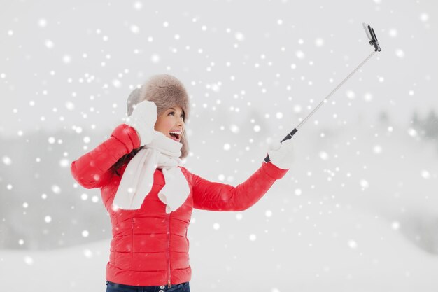 Foto mujer feliz con un palo de selfie al aire libre en invierno