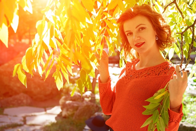 Una mujer feliz en un parque de otoño con un sombrero con una hoja de arce al sol