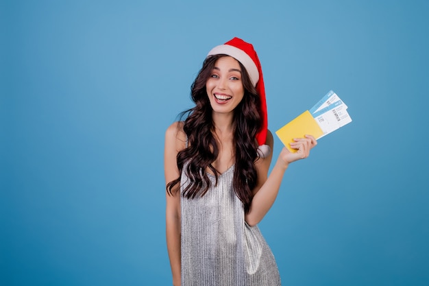 Mujer feliz con pasajes de avión y pasaporte con sombrero de Navidad aislado sobre azul