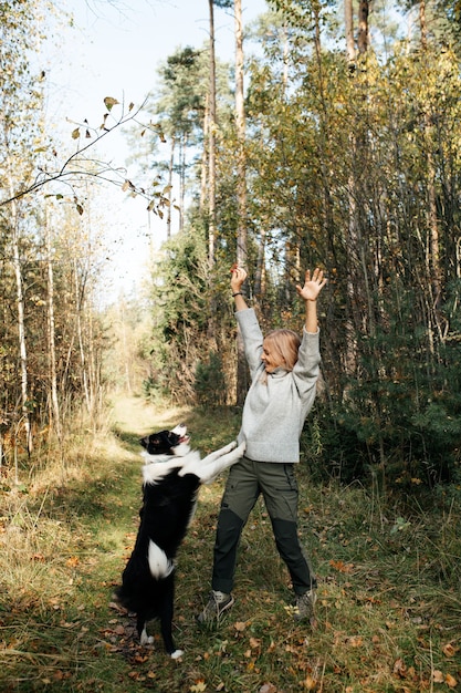 Mujer feliz y perro border collie blanco y negro en el bosque de otoño