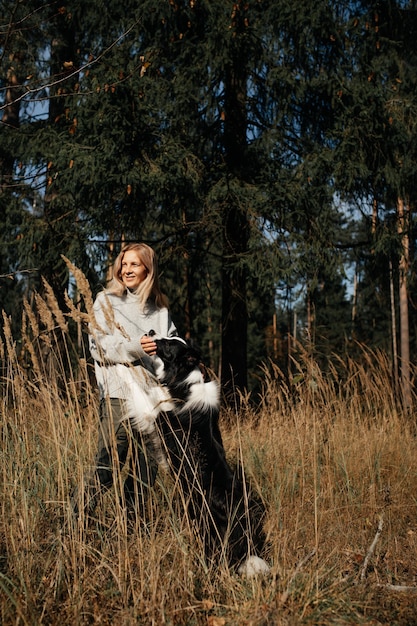 Mujer feliz y perro border collie blanco y negro en el bosque de otoño