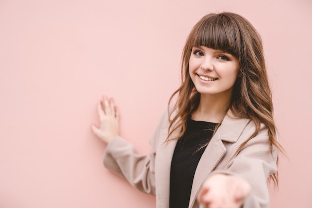 La mujer feliz de pie en el fondo de la pared rosa