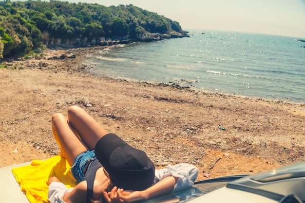 Mujer feliz en la playa de verano del mar sentada en el capó del coche