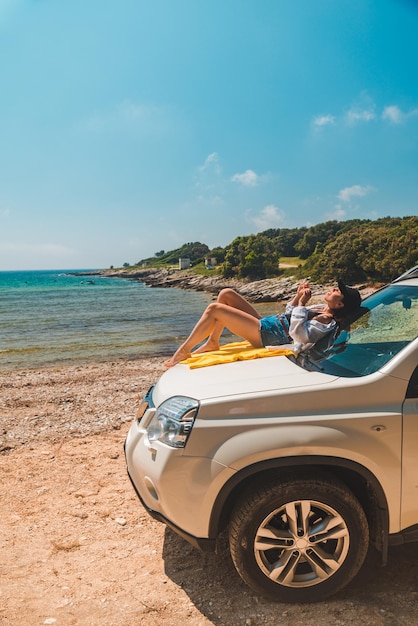 Mujer feliz en la playa de verano del mar sentada en el capó del coche