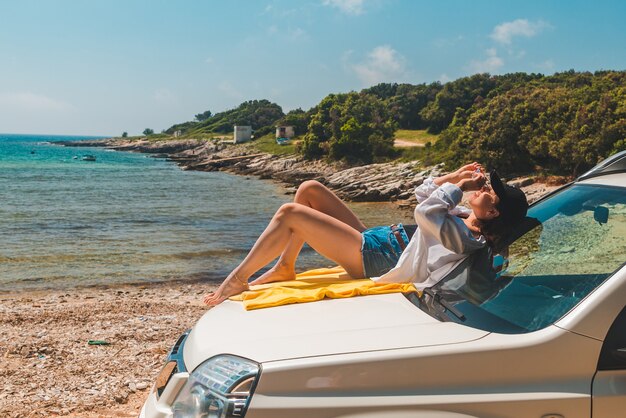 Mujer feliz en la playa de verano de mar sentado en el capó del coche concepto de vacaciones
